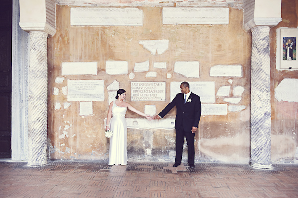 the happy couple standing in front of historic building holding hands - wedding photo by top Rome based destination wedding photographer Rochelle Cheever, Rome Weddings Photography